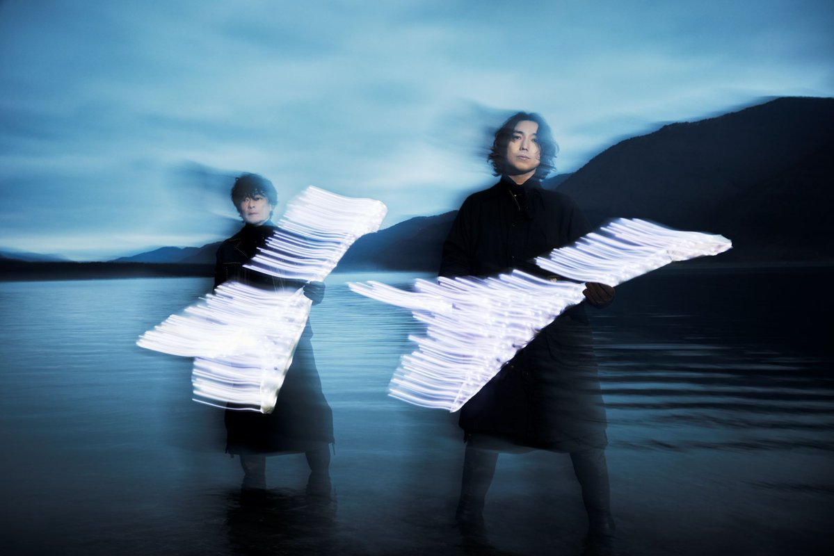 Artist photo for THE SPELLBOUND x BOOM BOOM SATELLITES showing two figures in black standing in shallow water at dusk